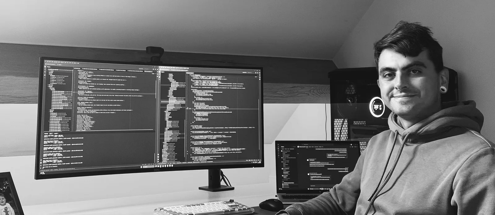 Douwe aan zijn bureau, naast een beeldscherm en laptop met code.